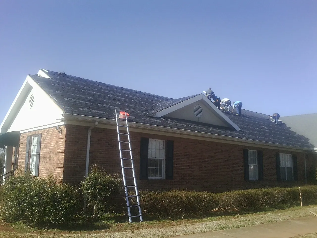 Crew tearing shingles off a brick ranch roof with a ladder set — Emergency Roof Repair work by our crew in Funston