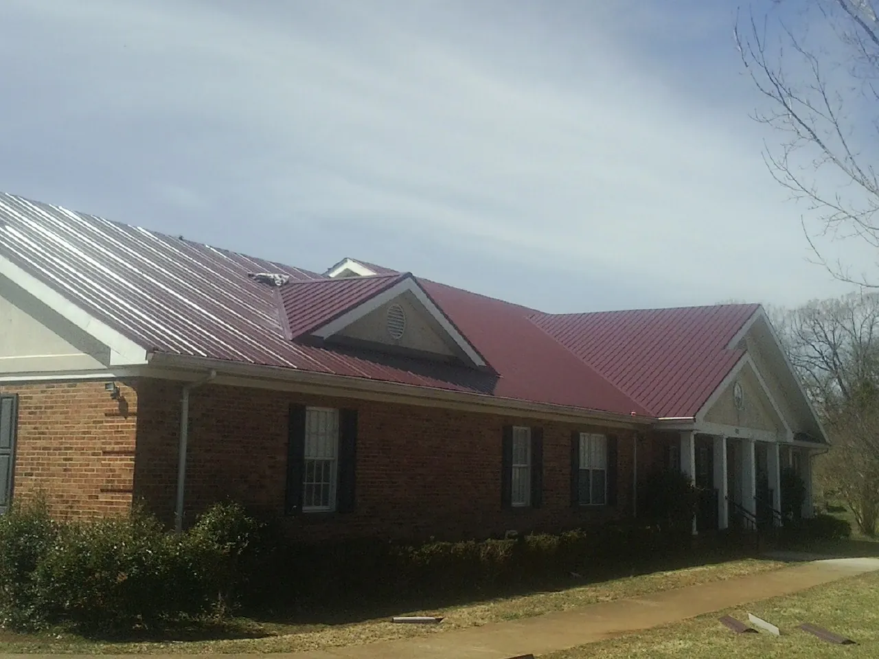 Red metal roof with gabled entries on a long brick building, from a Hail Damage Roof Repair job in Funston