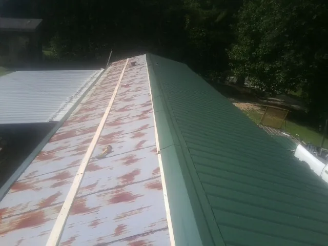 Old rusted panels beside newly installed green metal roofing — Wind Damage Roof Repair by Roofing Brothers in Funston