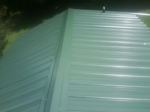 New green metal panels meeting at the ridge of a roof — Flat Roof Repair work by our crew in Funston