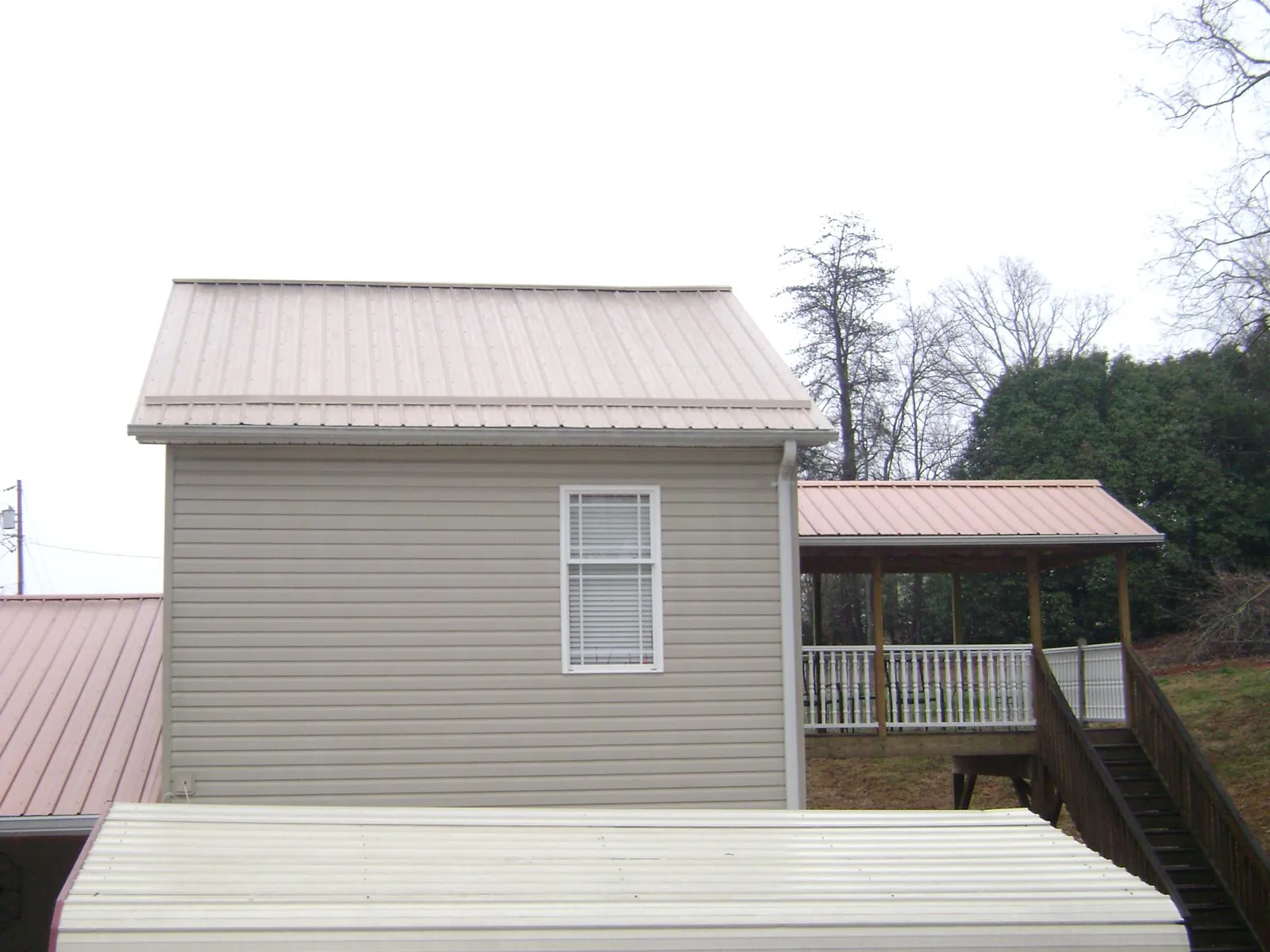 Tan metal roofs on a two story addition and attached porch, from a Roof Replacement job in Funston